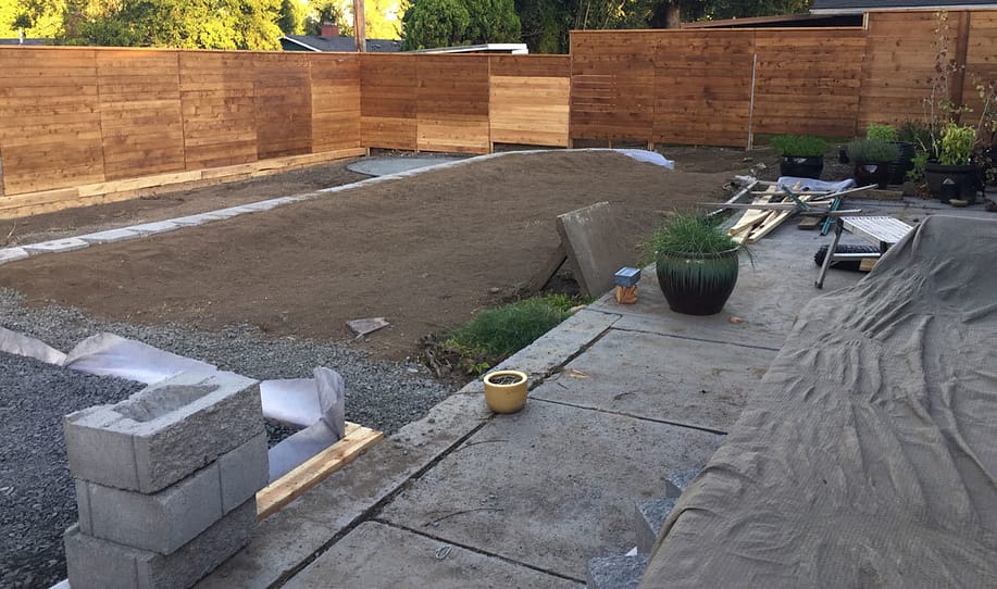 Photo of our half-finished backyard landscaping project. Unfinished retaining wall, materials left everywhere and dirt with no grass or mulch